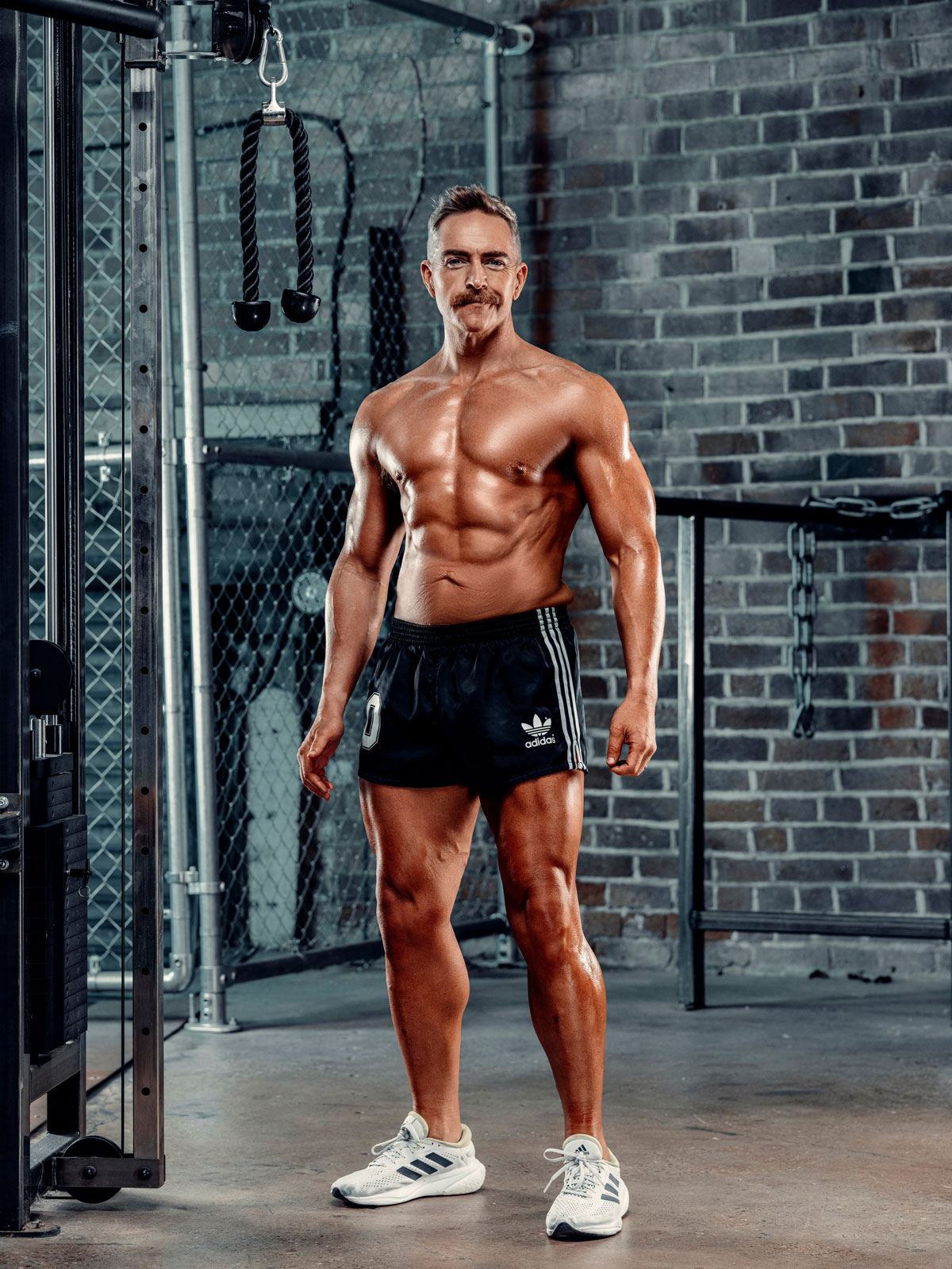 Coach is posing for a photo in a gym, shirtless.